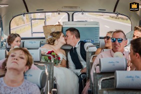 Een echtpaar uit Essen deelt een spontane kus op de achterste rij van een vintage bus terwijl het huwelijksfeest onscherp op de voorgrond zit.